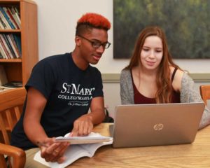 Two students studying in library classroom with laptop.