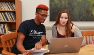 Two students studying in library classroom with laptop.