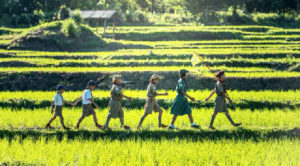 six children walk in a straight line across fields of green grass